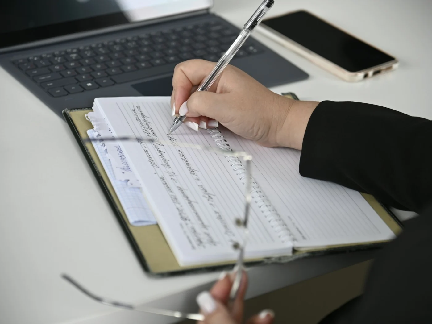 Writing notes beside a laptop while planning content