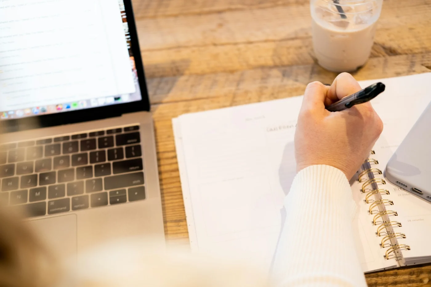 Someone writing audit notes in a notebook next to a laptop