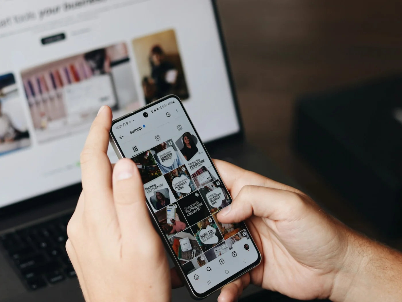 Someone browsing a business Instagram profile on a phone in front of a laptop